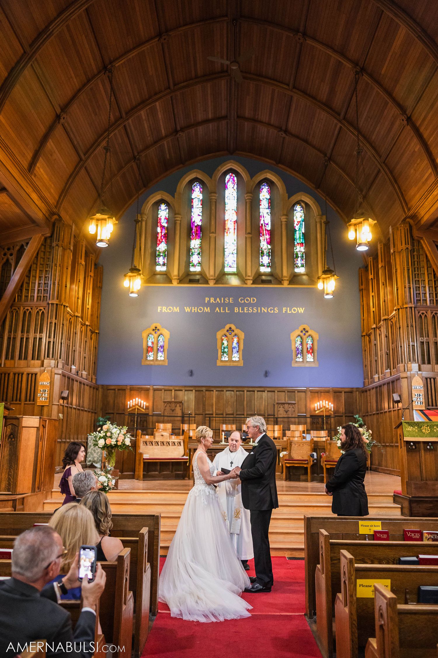 Wedding ceremony in progress under vaulted church ceiling with colorful stained glass windows.