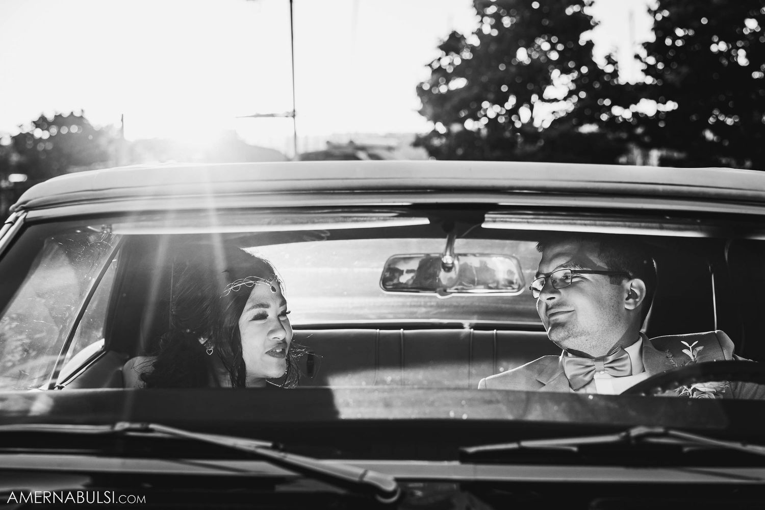 Black and white photo of a couple sharing a joyful moment in a vintage car.
