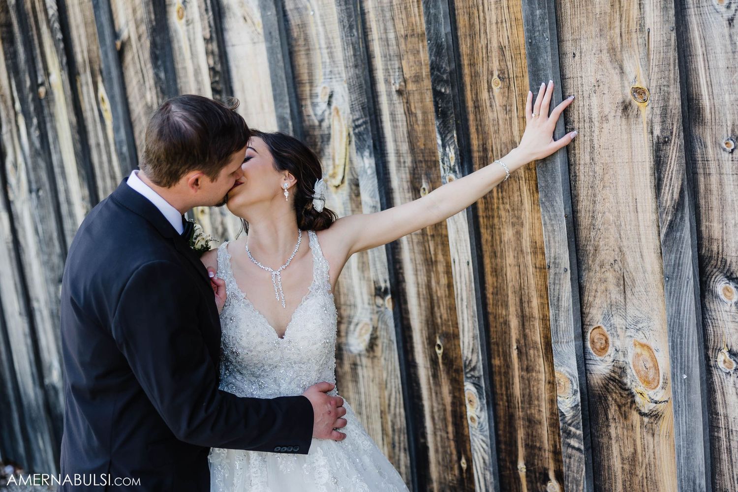 Romantic wedding moment captured against rustic wooden wall with bride's dramatic pose.