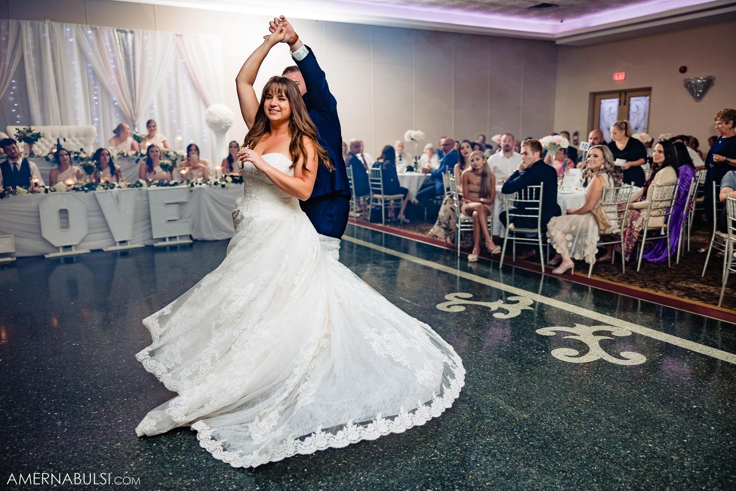 Newlyweds perform romantic dance move on reception floor with guests watching.
