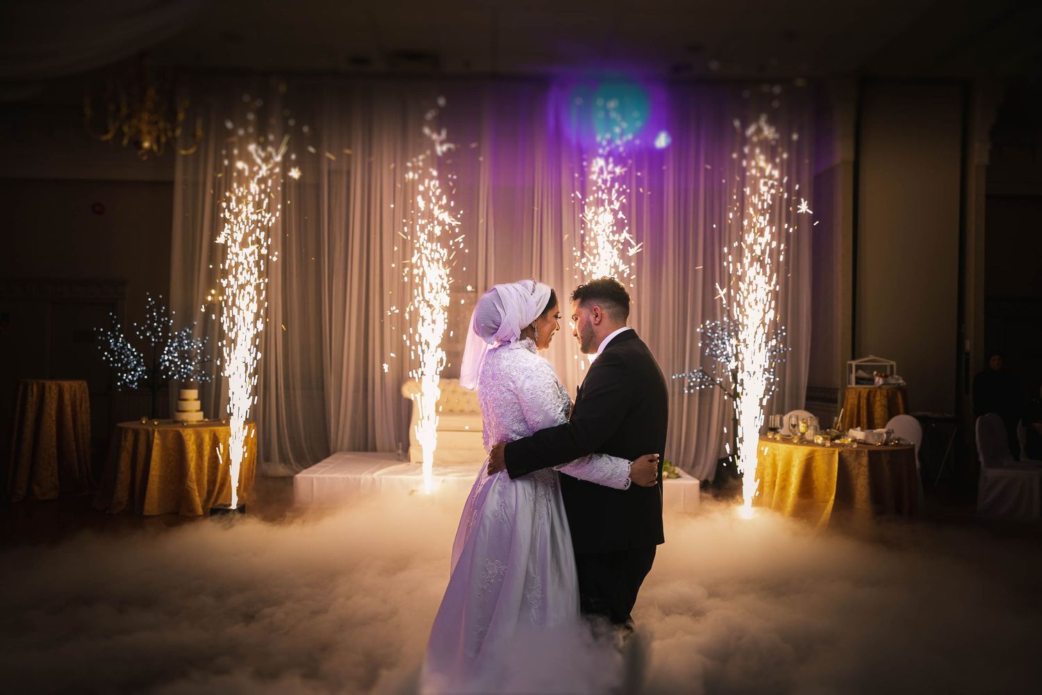 Newlyweds share their first dance under dramatic sparkler effects and purple lighting at their wedding reception.