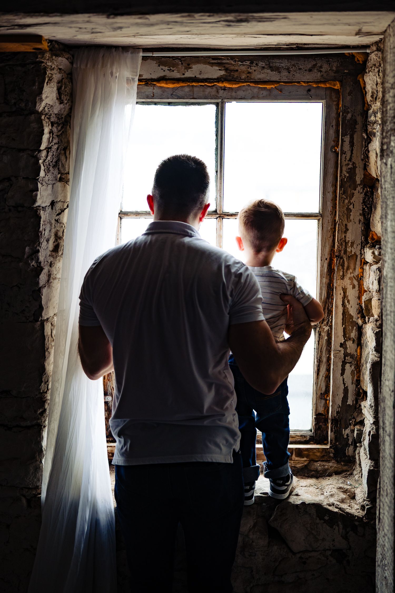 Silhouette of parent and child looking through weathered window frame.