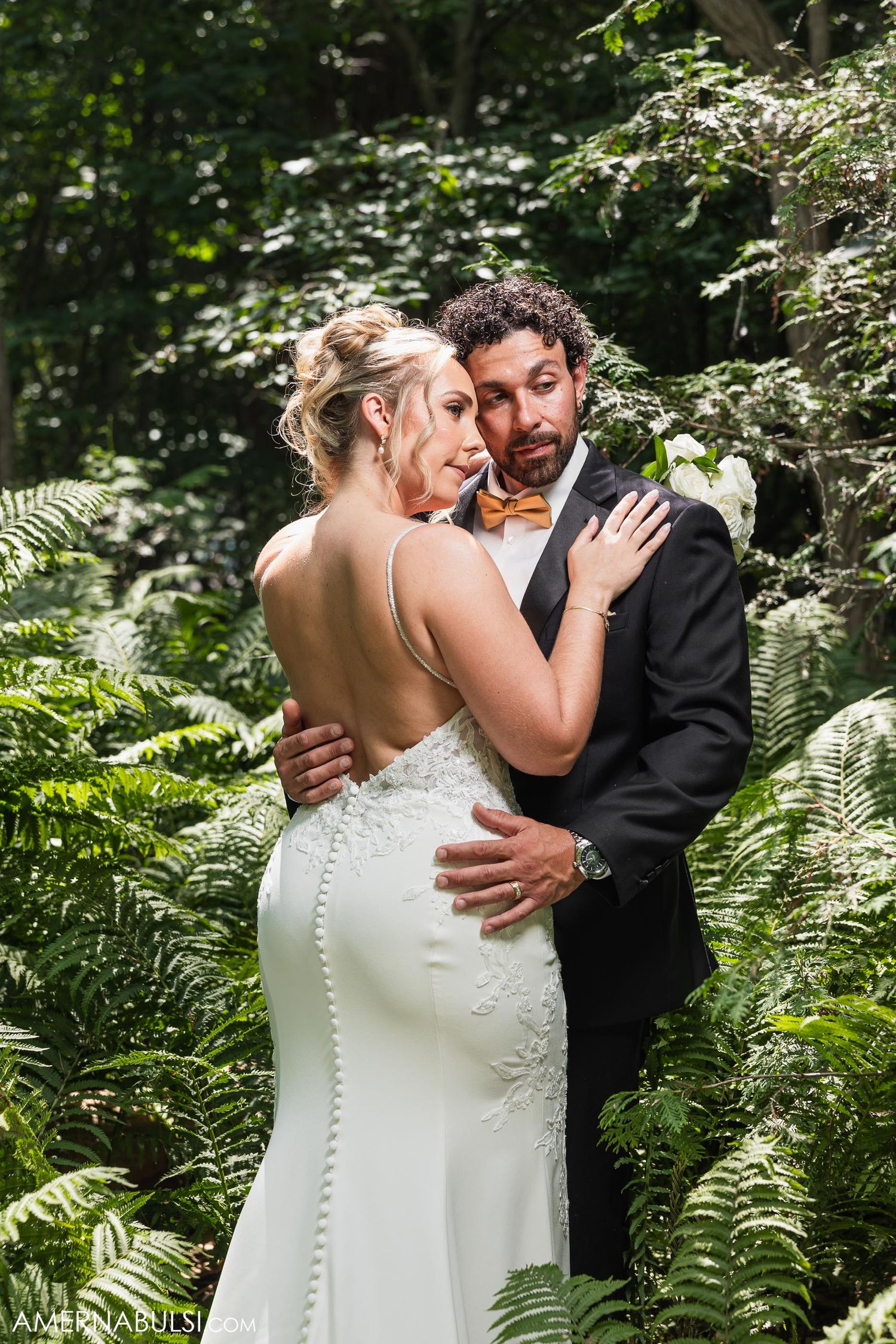 Intimate portrait of couple embracing in woodland setting with ferns and dappled sunlight.
