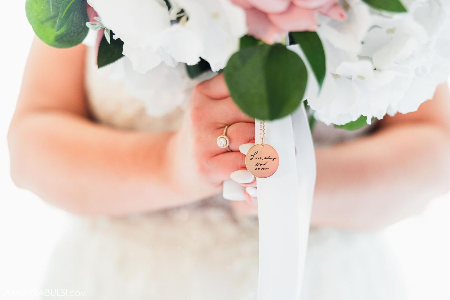 Close-up of wedding rings held against white bouquet ribbon.