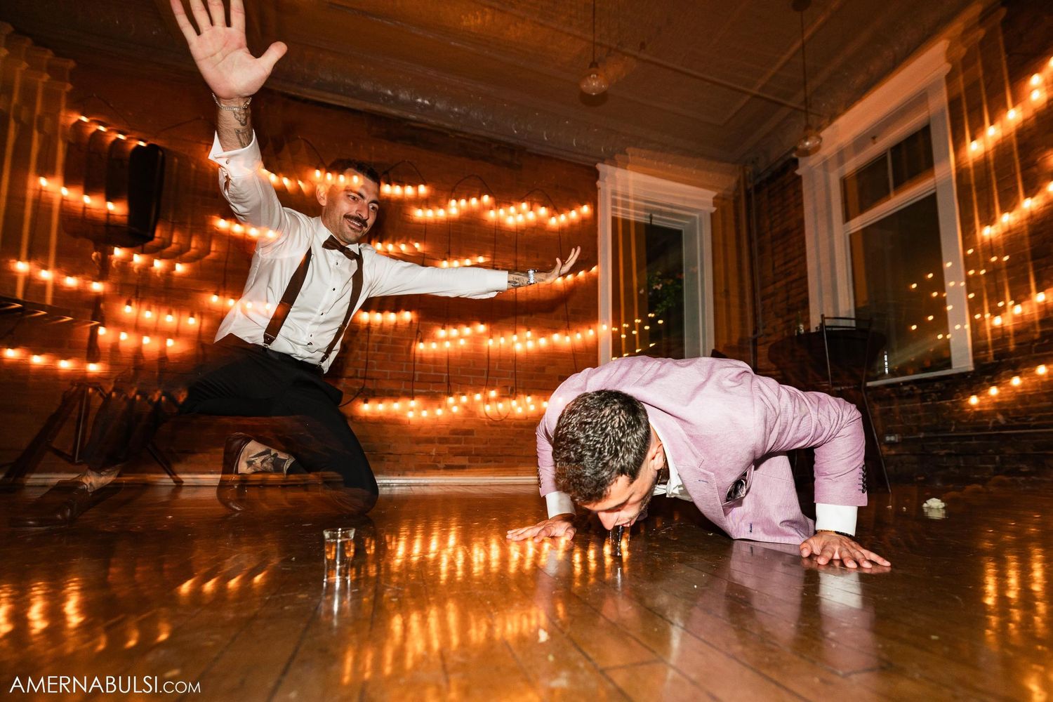 Two guests dance energetically on a wooden dance floor under glowing string lights.