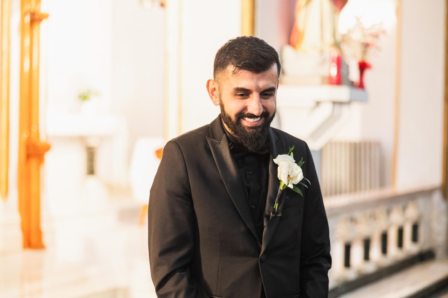 Groom in dark suit with boutonniere smiles warmly during wedding ceremony.