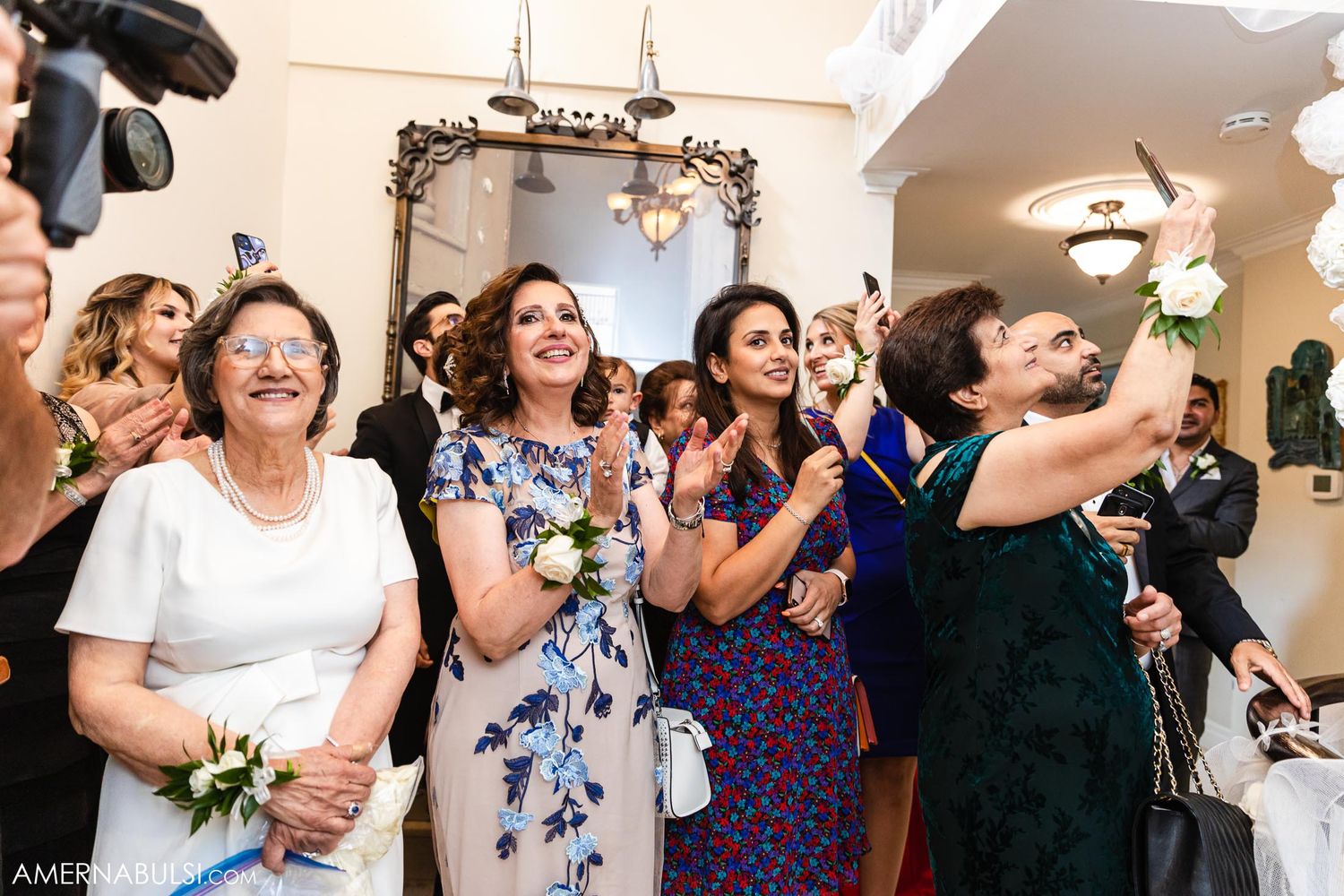 Wedding guests react with joy and emotion while watching ceremony in an ornate room.