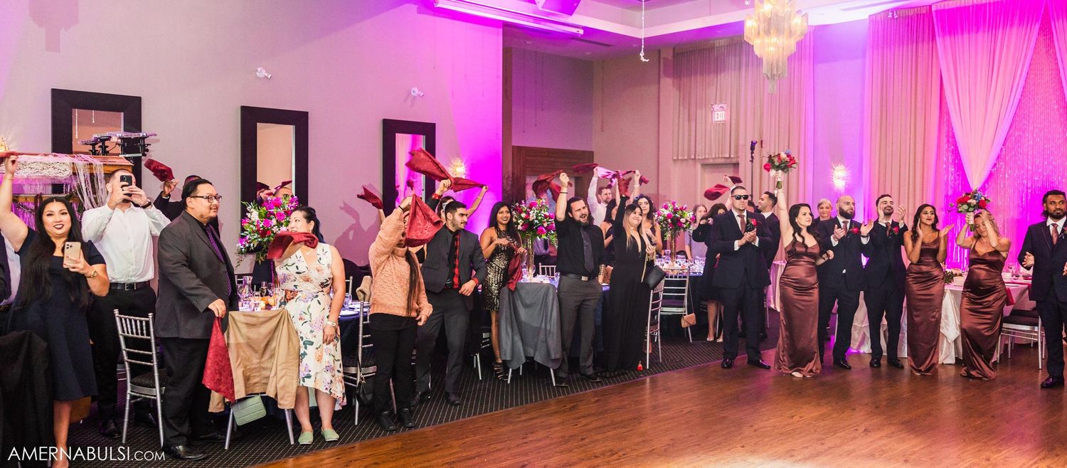 Wedding reception crowd watching celebration in elegant ballroom with pink uplighting.