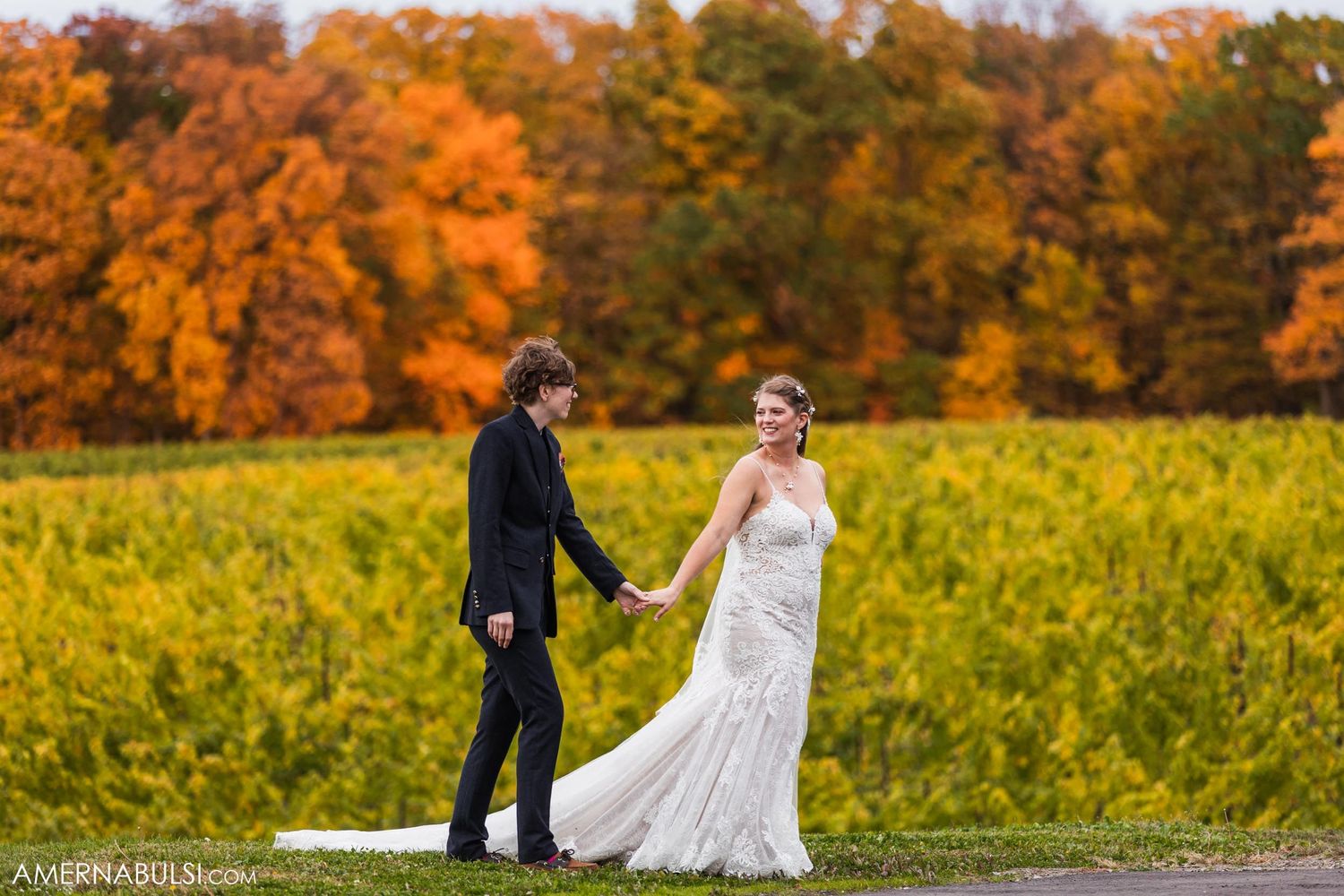 Newlyweds walking hand in hand through autumn vineyard with orange fall colors.
