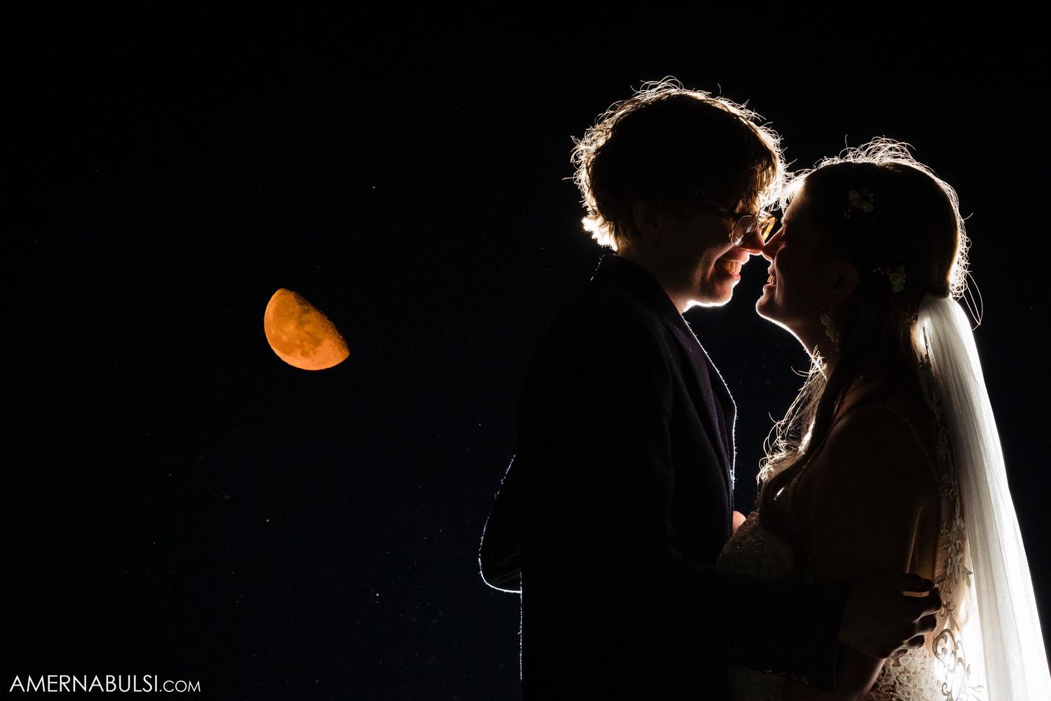 Romantic silhouette against orange crescent moon creating dramatic nighttime wedding portrait.