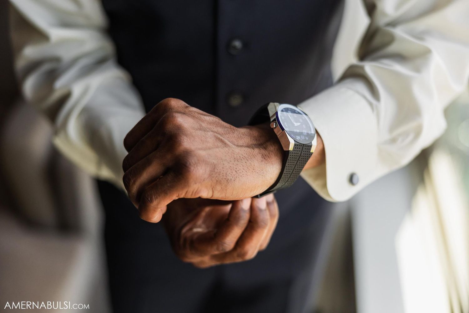 Close-up of groom's hands adjusting silver watch with white shirt cuffs.