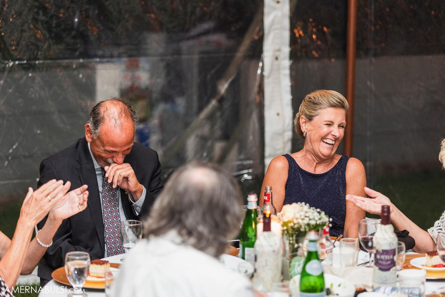 Wedding guests laughing and enjoying dinner at an outdoor reception table.