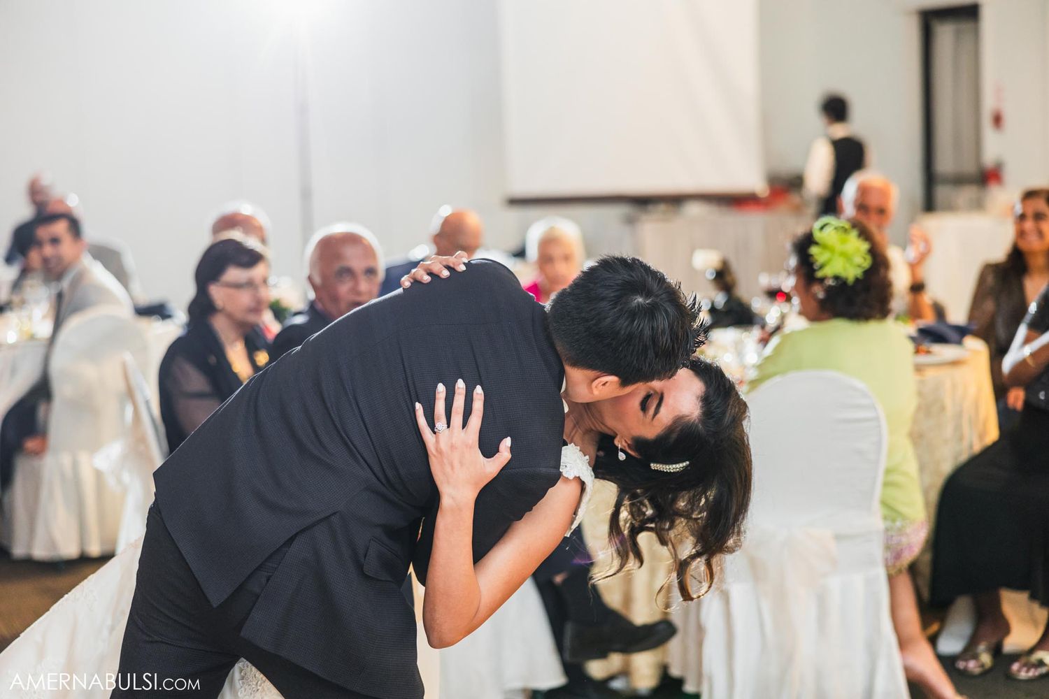 Couple shares an intimate dance moment during wedding reception with guests in background.