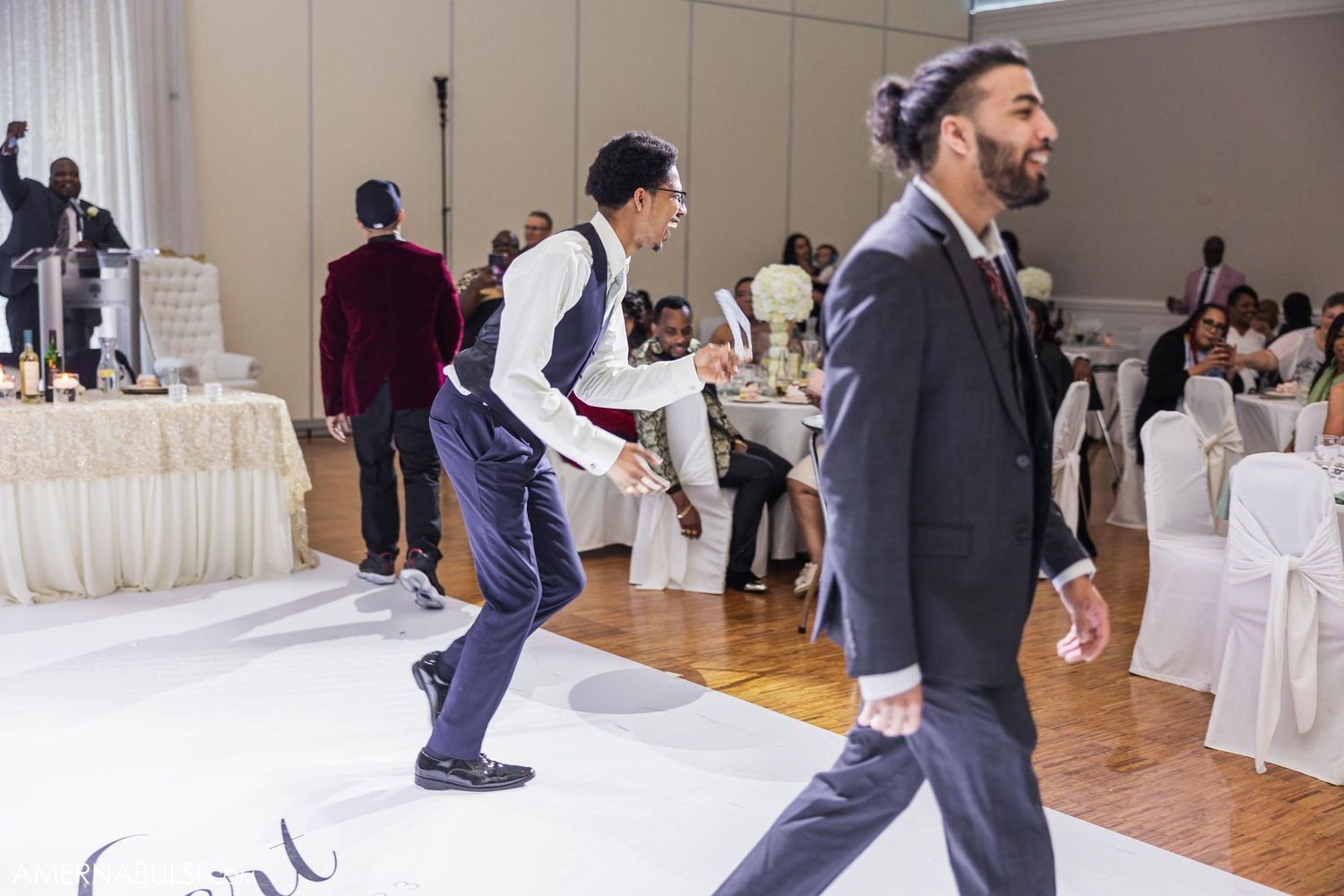 Guests dancing and celebrating at an elegant wedding reception in a ballroom with white decor.