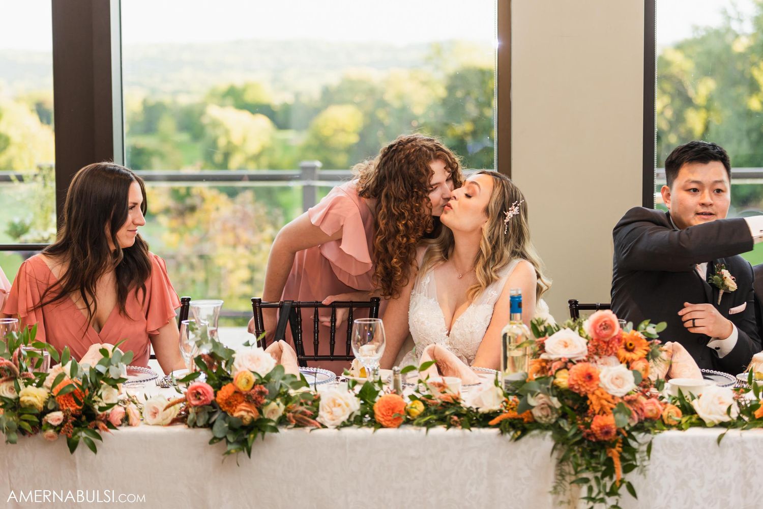 Wedding party shares laughs and embraces at decorated reception head table.