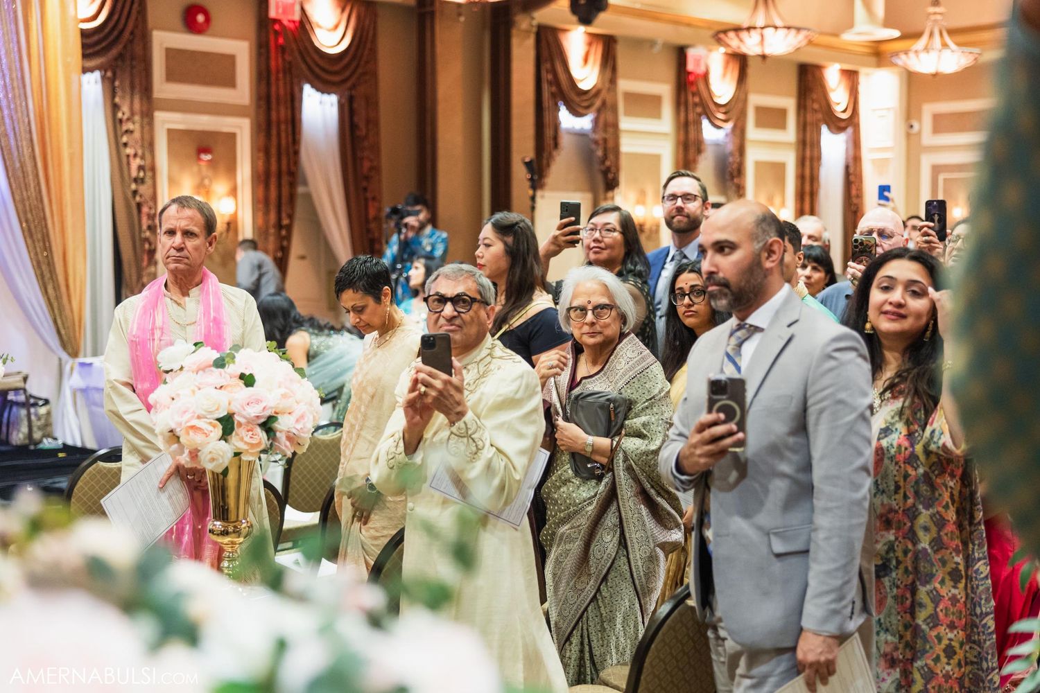 Wedding attendees watch and record a touching moment during a traditional Indian ceremony in an elegant ballroom.