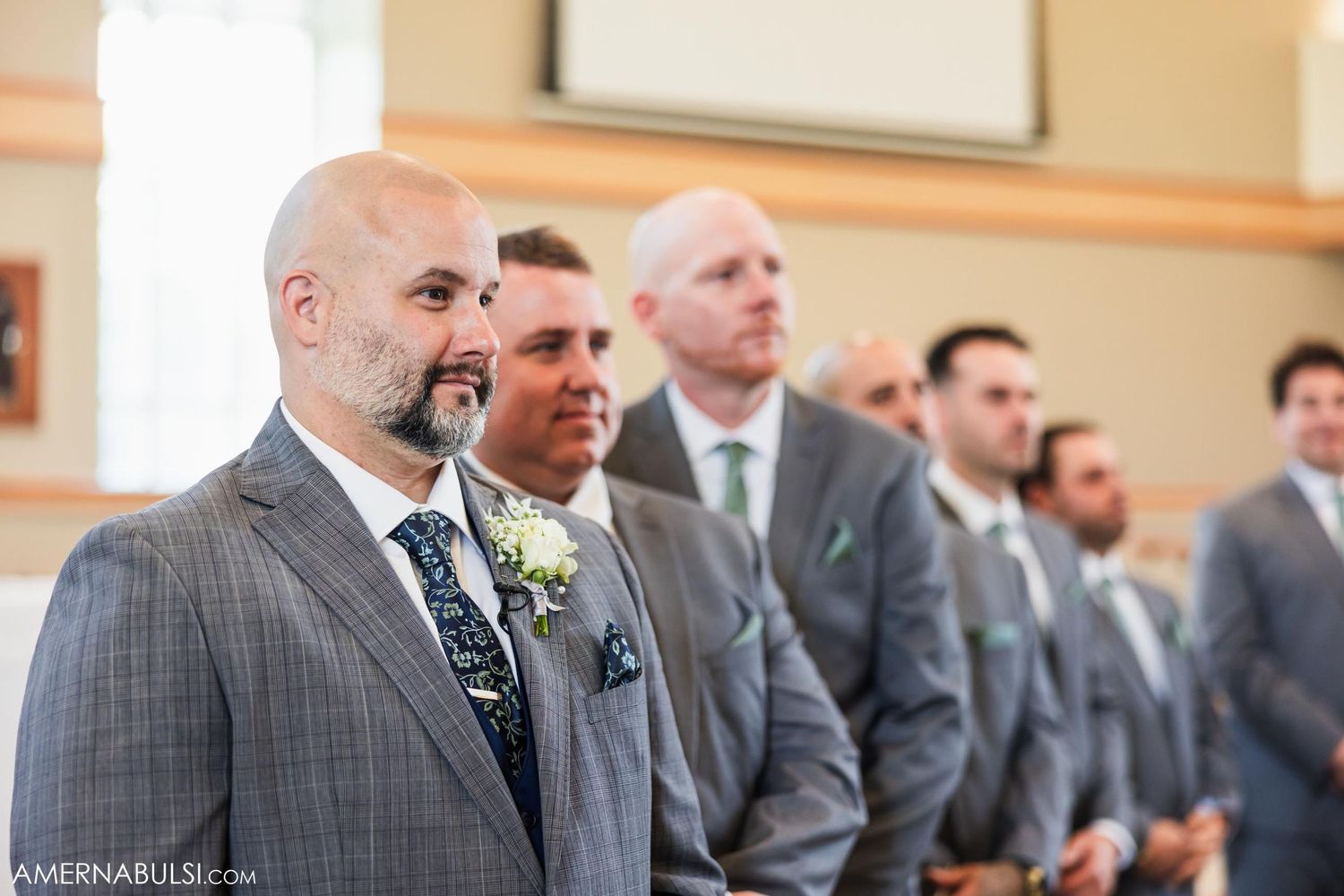 Groomsmen stand at attention during a wedding ceremony wearing matching grey suits.
