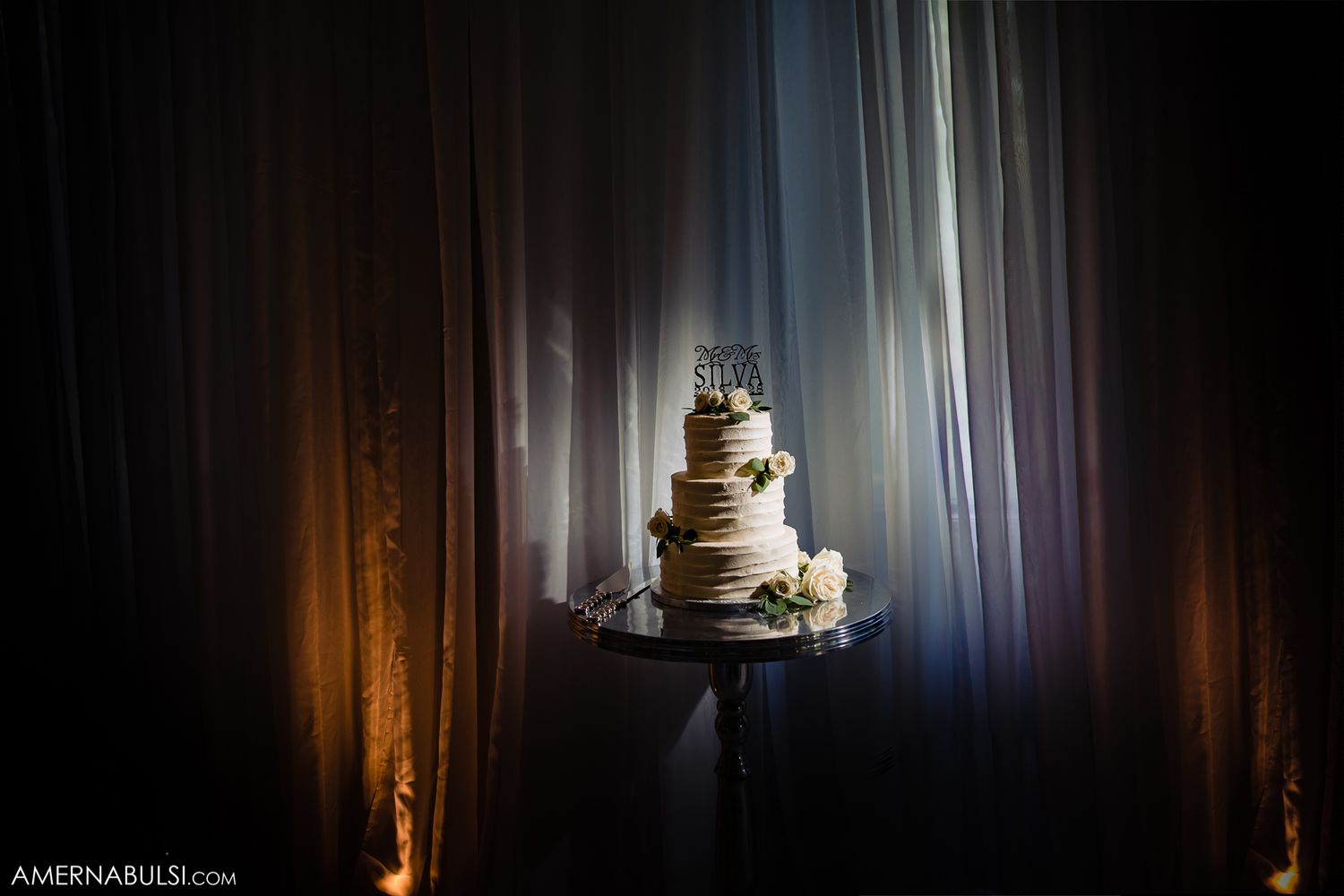 Wedding cake table decorated with white floral arrangements and soft lighting creates an elegant reception ambiance.