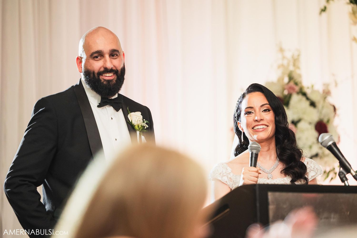 Formal wedding reception speech moment captured at an elegant venue with white decor.