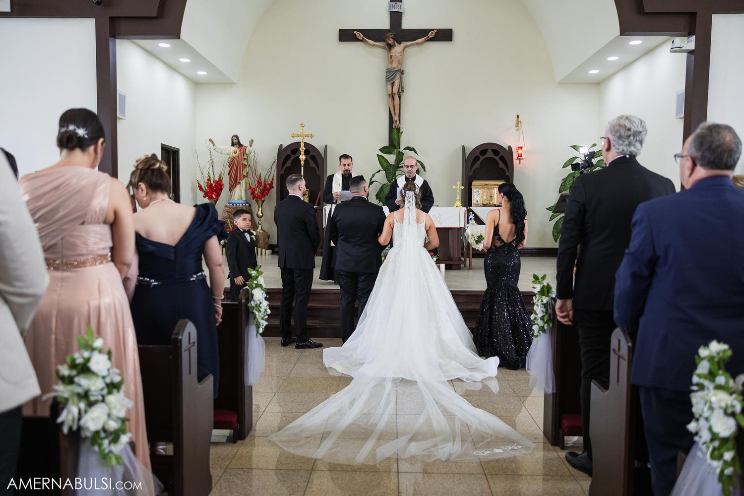 Wedding ceremony in a church with floral decorations and a long white veil trailing down the aisle.