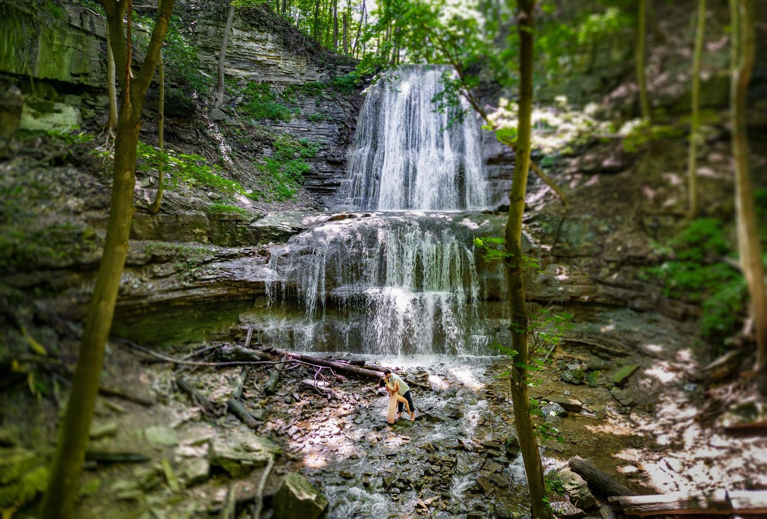 Serene waterfall cascades down rocky cliffs surrounded by green forest.