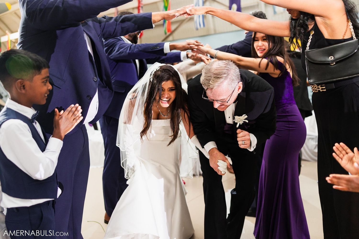Wedding party dances through a tunnel of guests raising their hands.