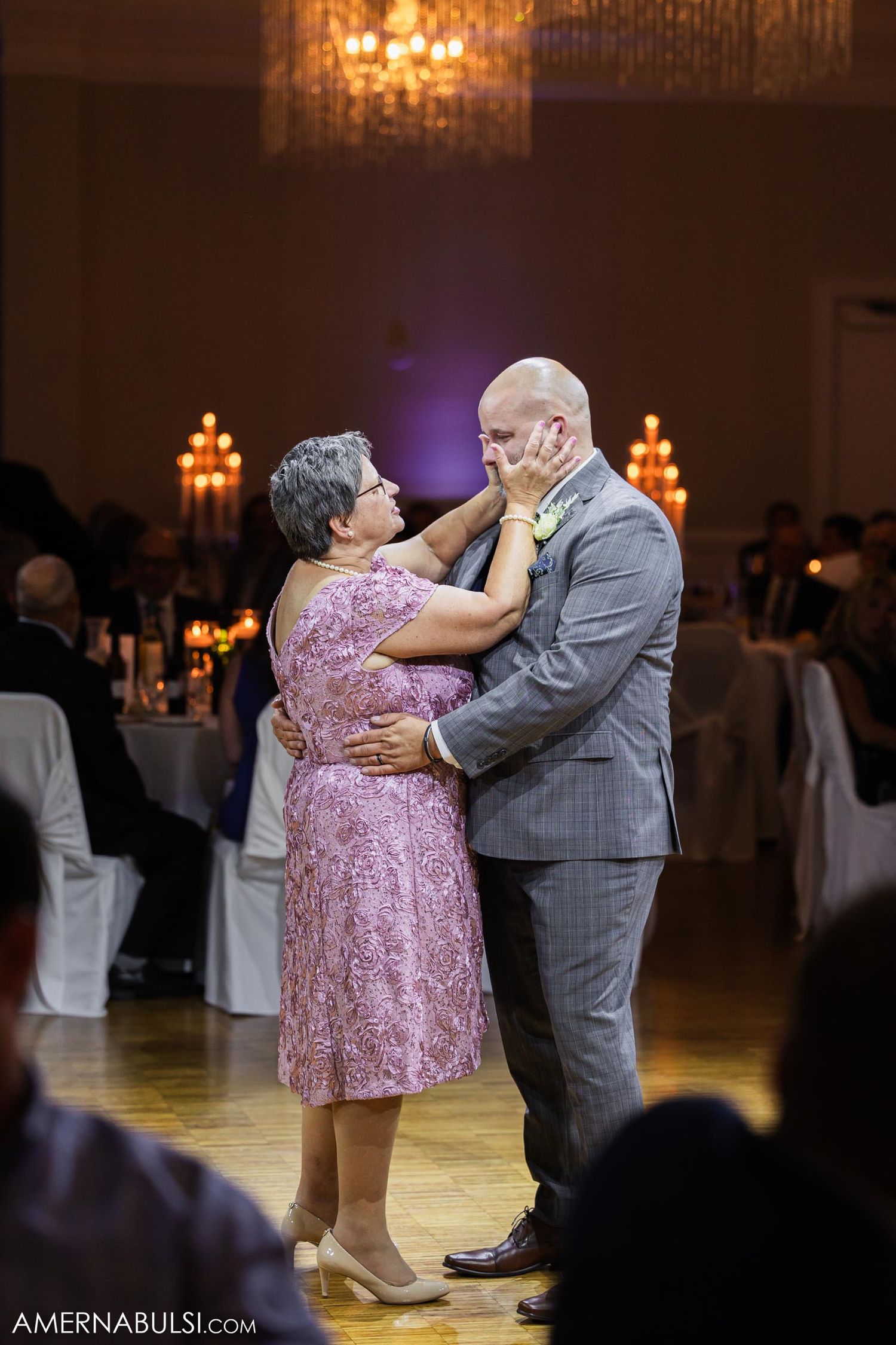 Couple sharing intimate dance moment under chandelier at formal event.