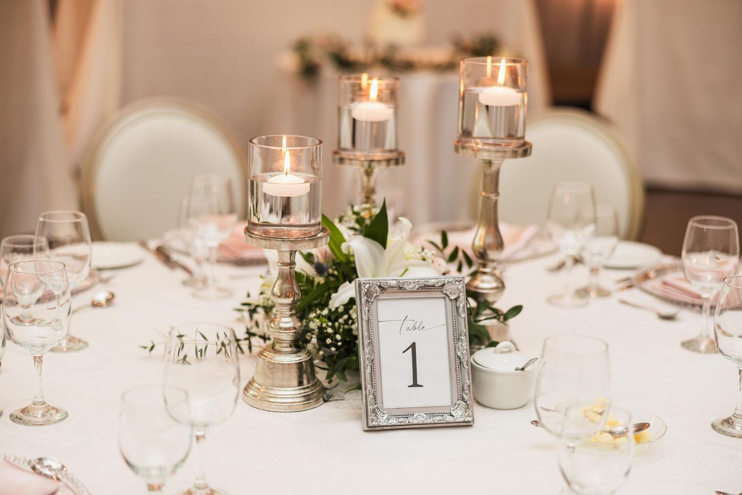 Elegant table centerpiece with glowing candles, table number one, and white floral arrangements.