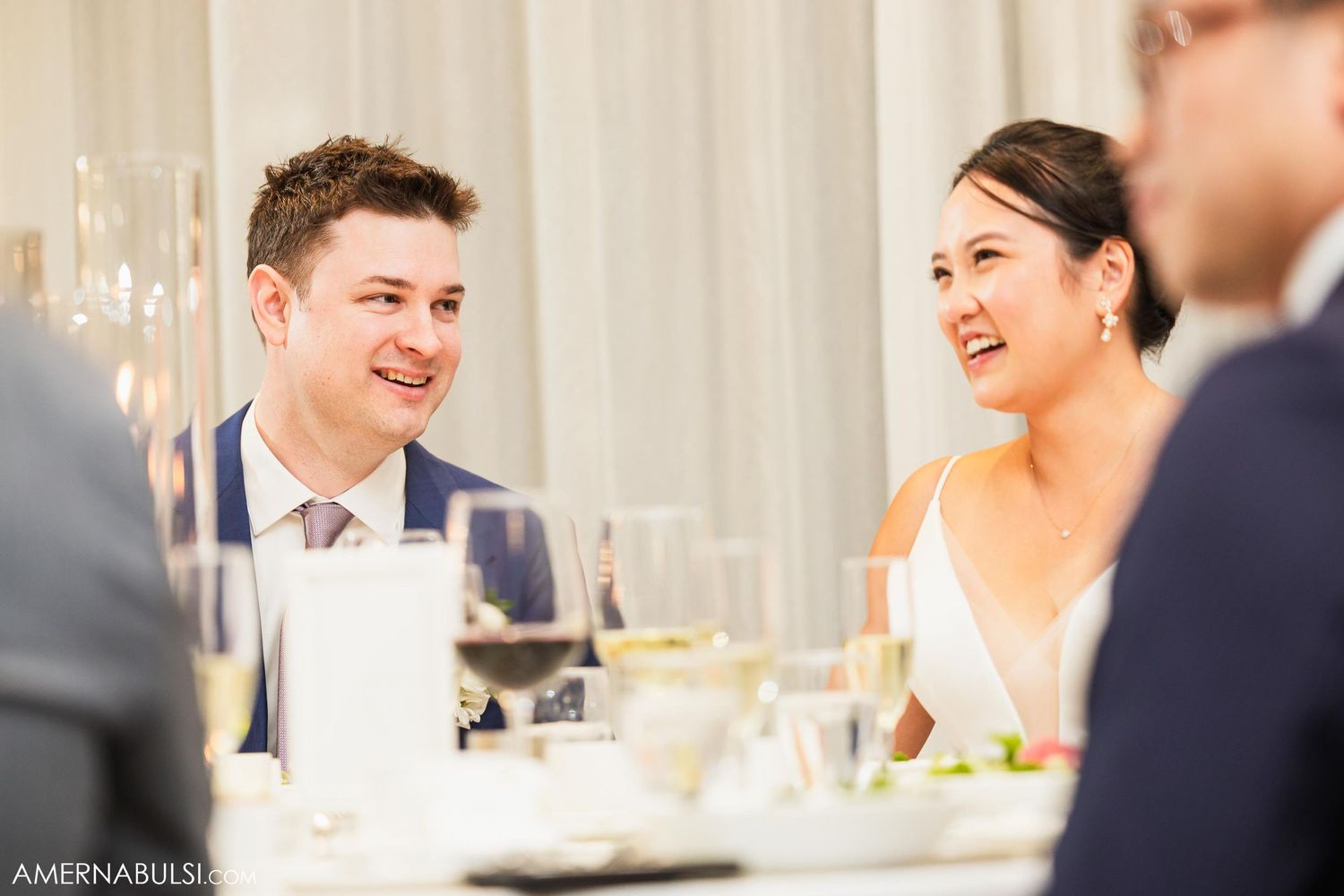 Candid reception moment of newlyweds sharing laughter at dinner table.