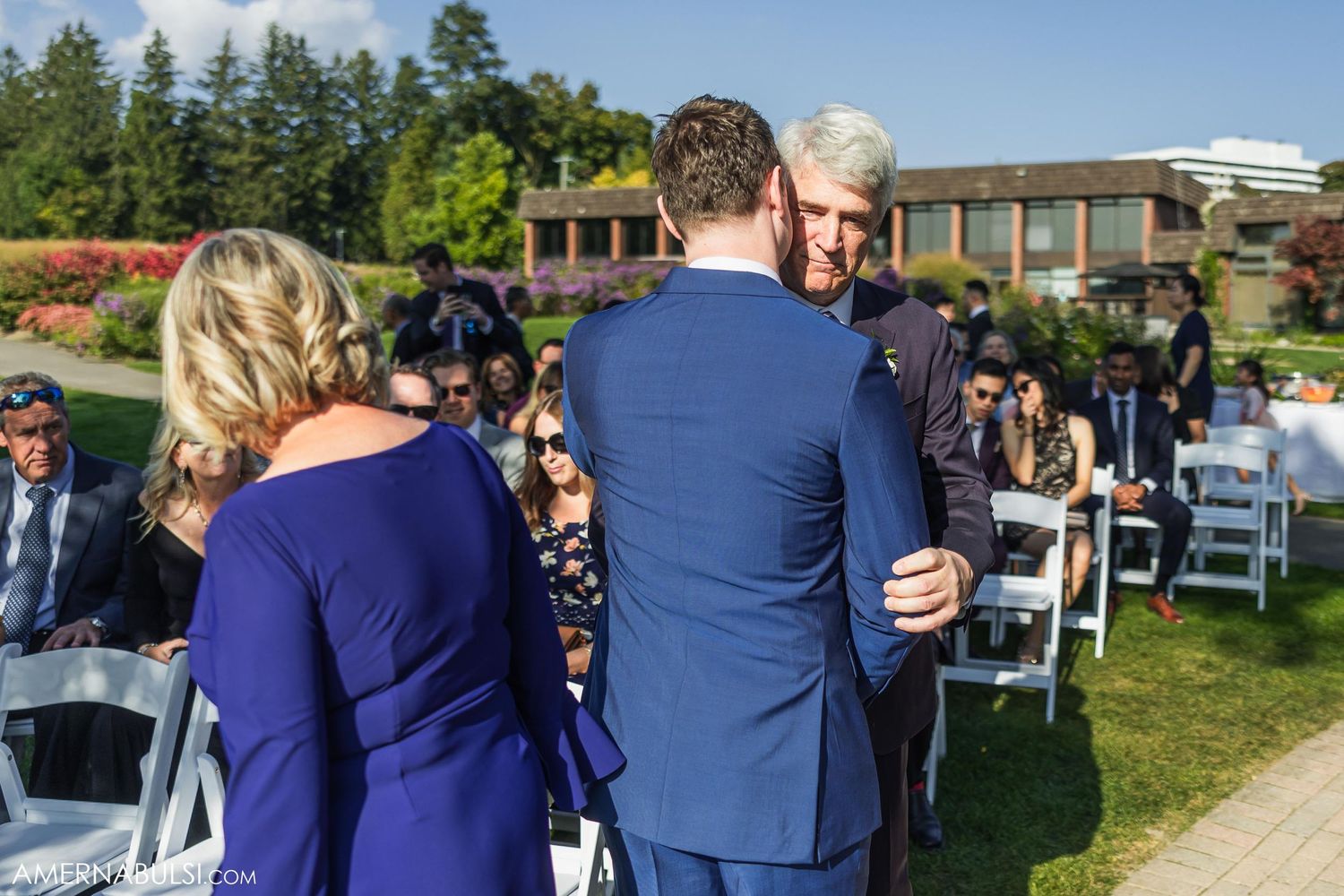 Outdoor wedding gathering with guests seated on white chairs under blue skies.