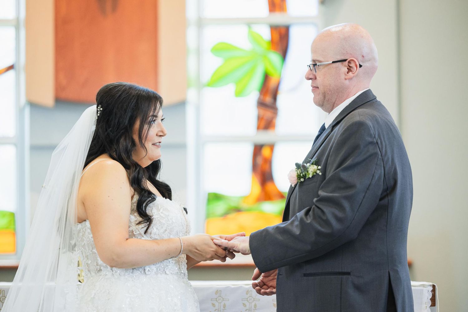 Wedding ceremony vow exchange with stained glass windows in background.