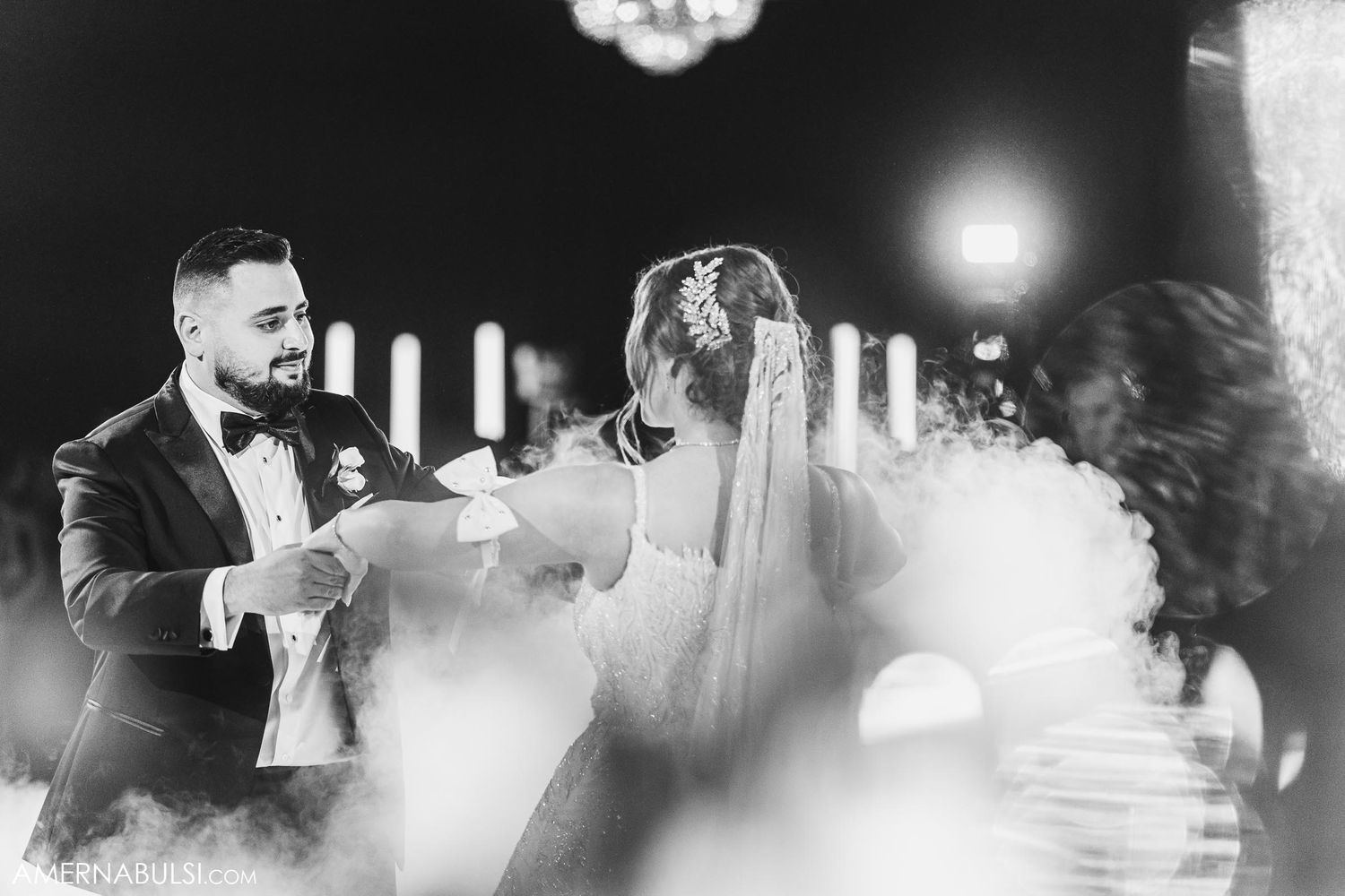 Black and white capture of couple dancing amid fog effects at wedding reception.