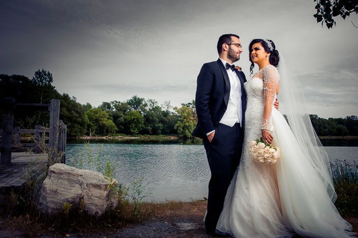 Elegant wedding portraits captured against a moody gray sky near a serene lake.