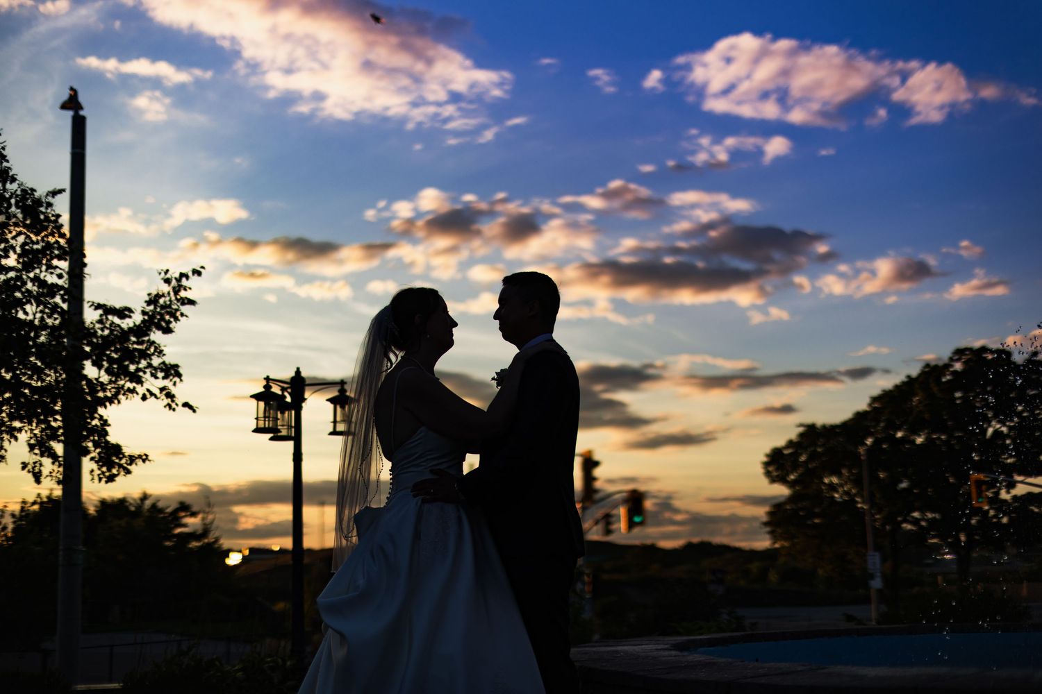 Romantic silhouette of bride and groom at sunset with colorful sky at outdoor wedding venue.