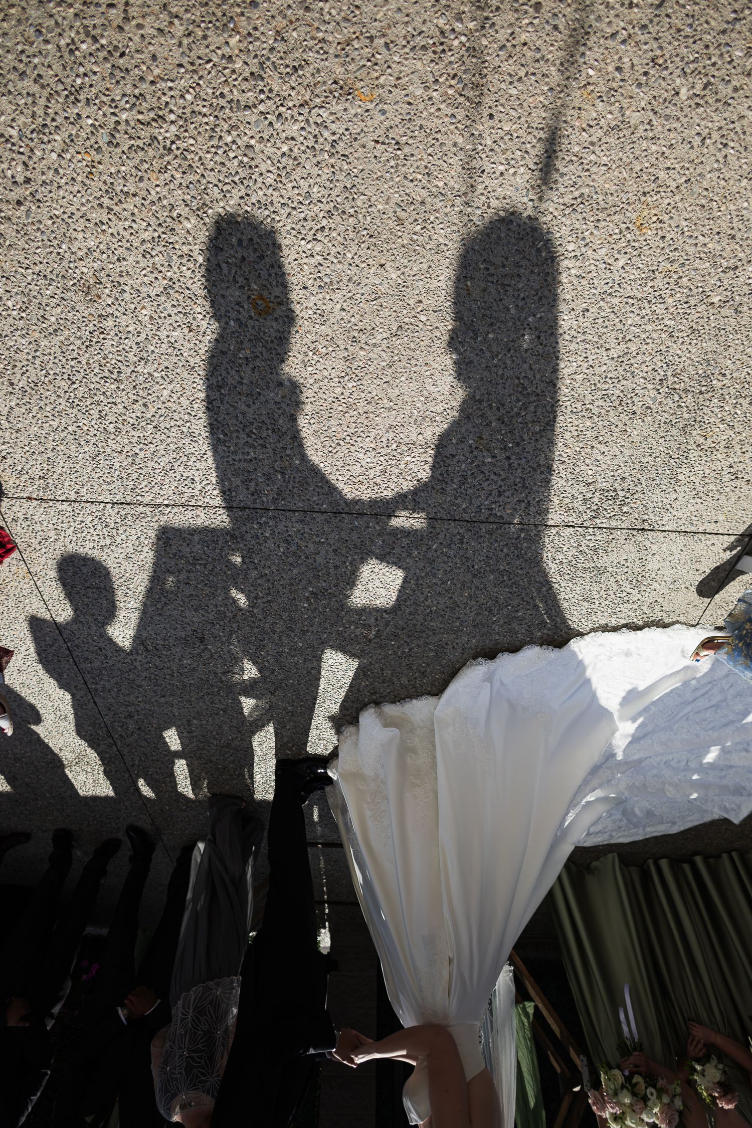 Shadows of bride and groom holding hands cast on textured wall during outdoor wedding ceremony.