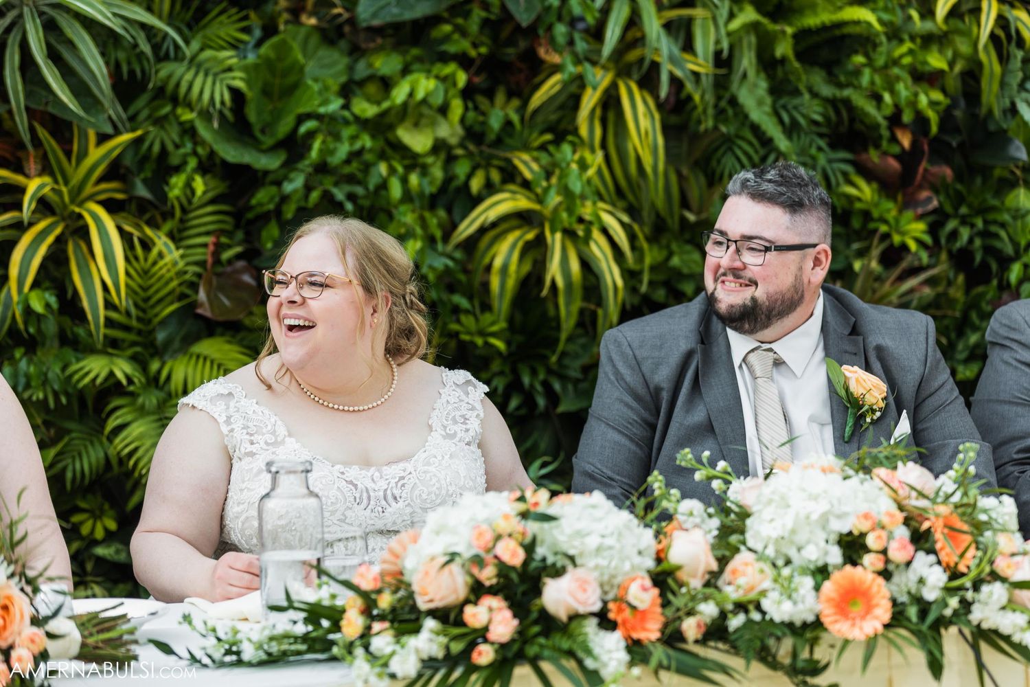 A couple shares a candid laughing moment at their wedding reception head table.