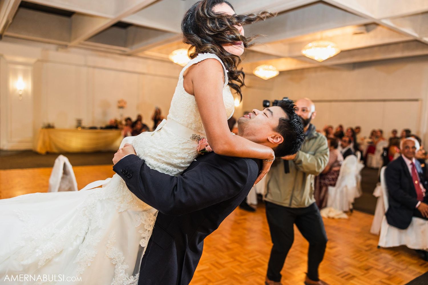 Playful wedding couple performs dramatic dance lift during reception celebration.