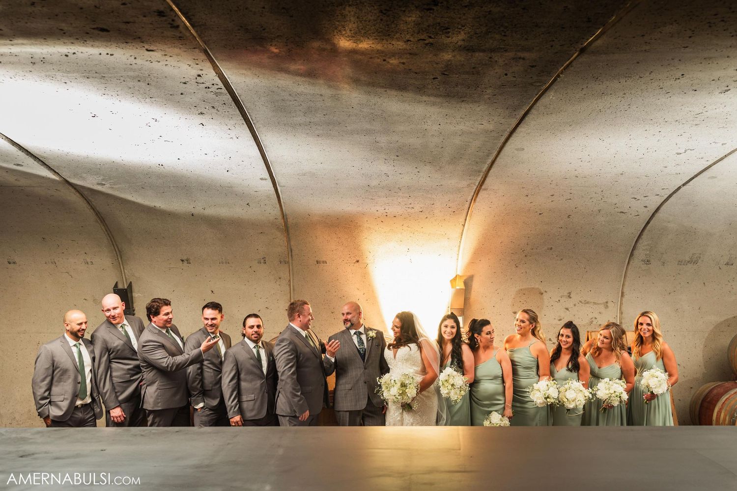 Wedding party poses in dramatic lighting under curved ceiling.