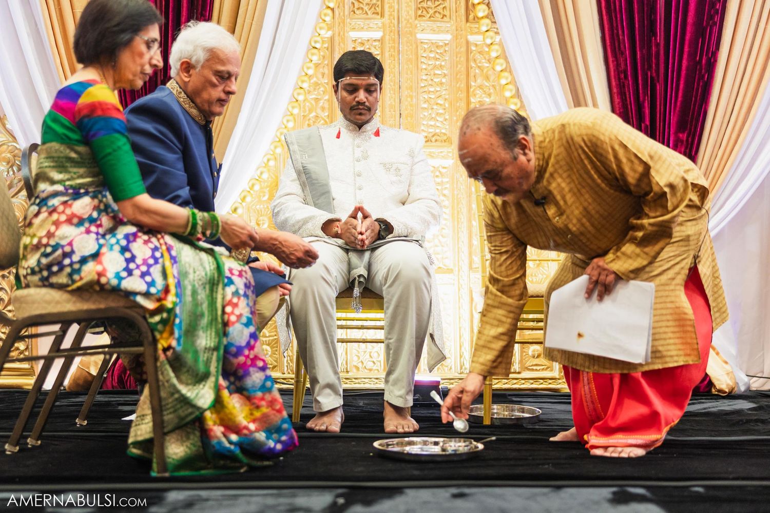 Traditional Indian wedding ceremony participants perform rituals on a raised black platform.