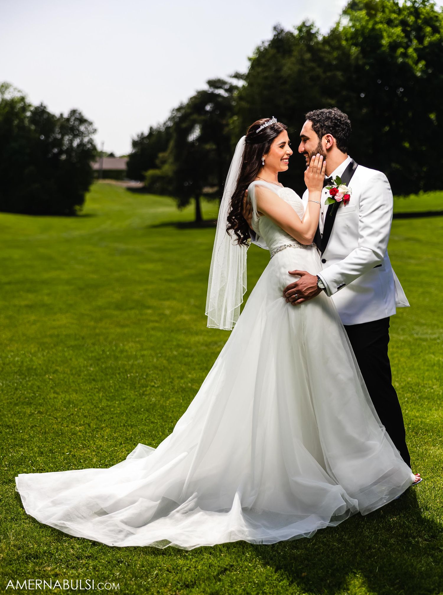 Romantic wedding portrait of couple in white attire embracing on manicured golf course.