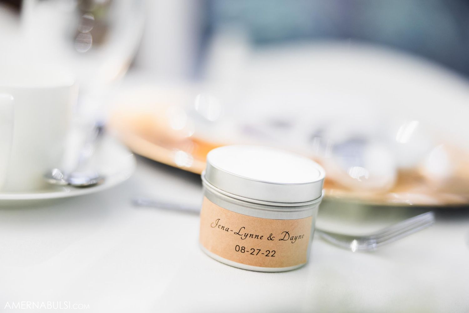Small labeled tin favor container sitting on white table with blurred table settings in background.