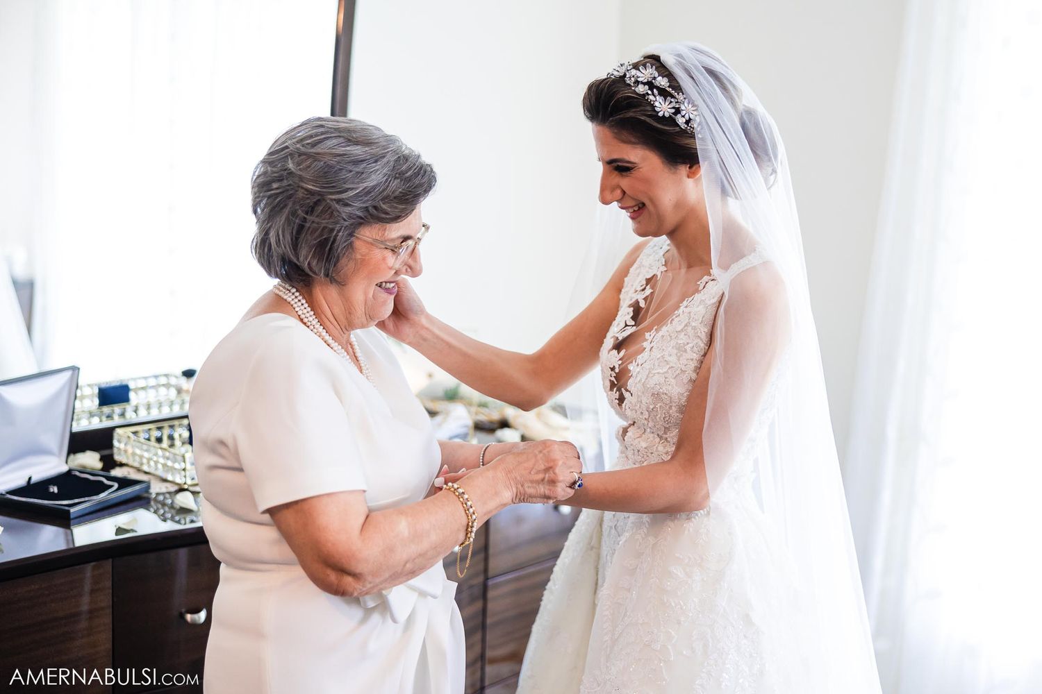 Emotional moment between bride in lace gown and older woman during wedding preparations.