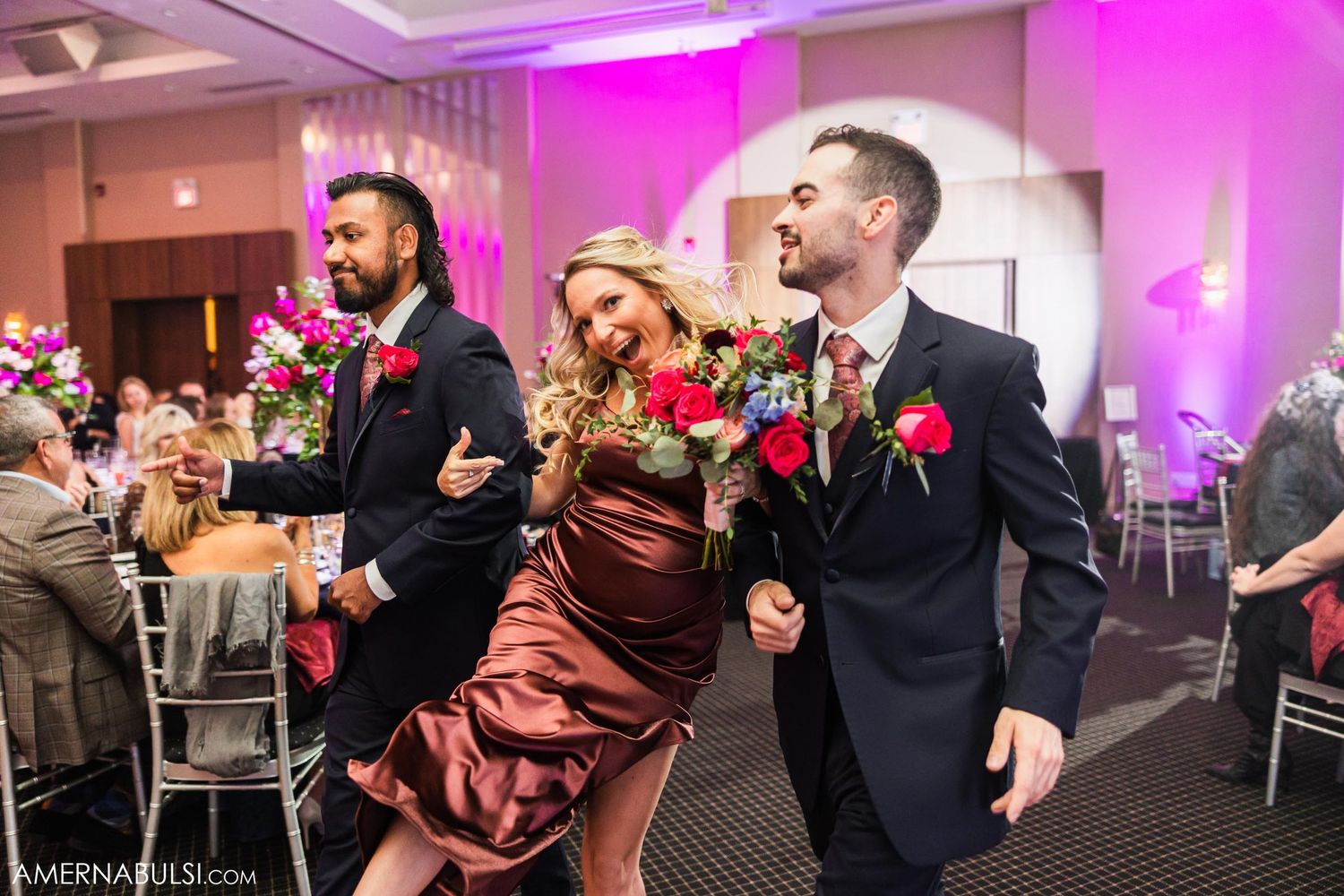 Wedding party dancing and laughing together at reception with burgundy and navy attire.