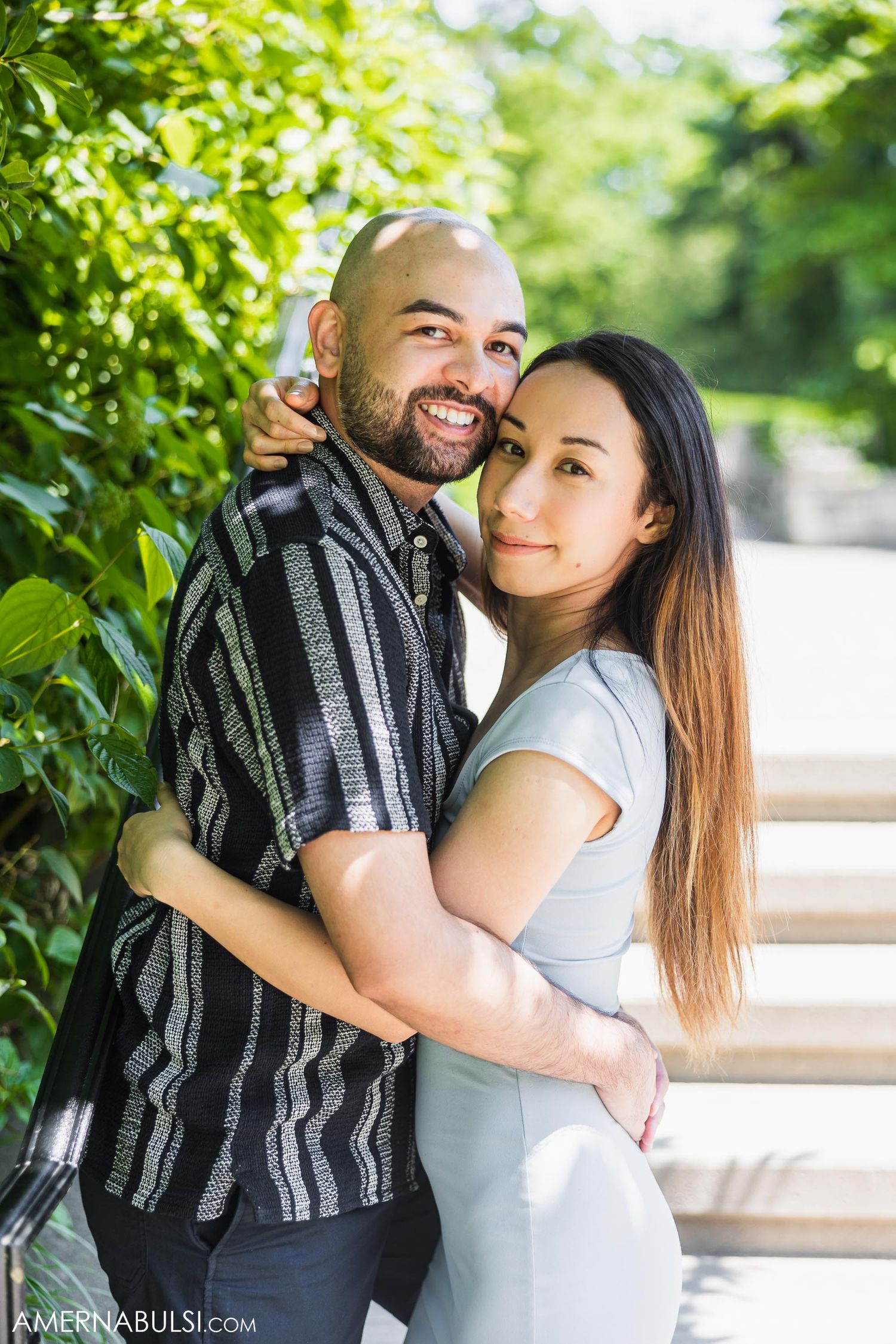 Affectionate couple embracing outdoors with green foliage and natural sunlight.