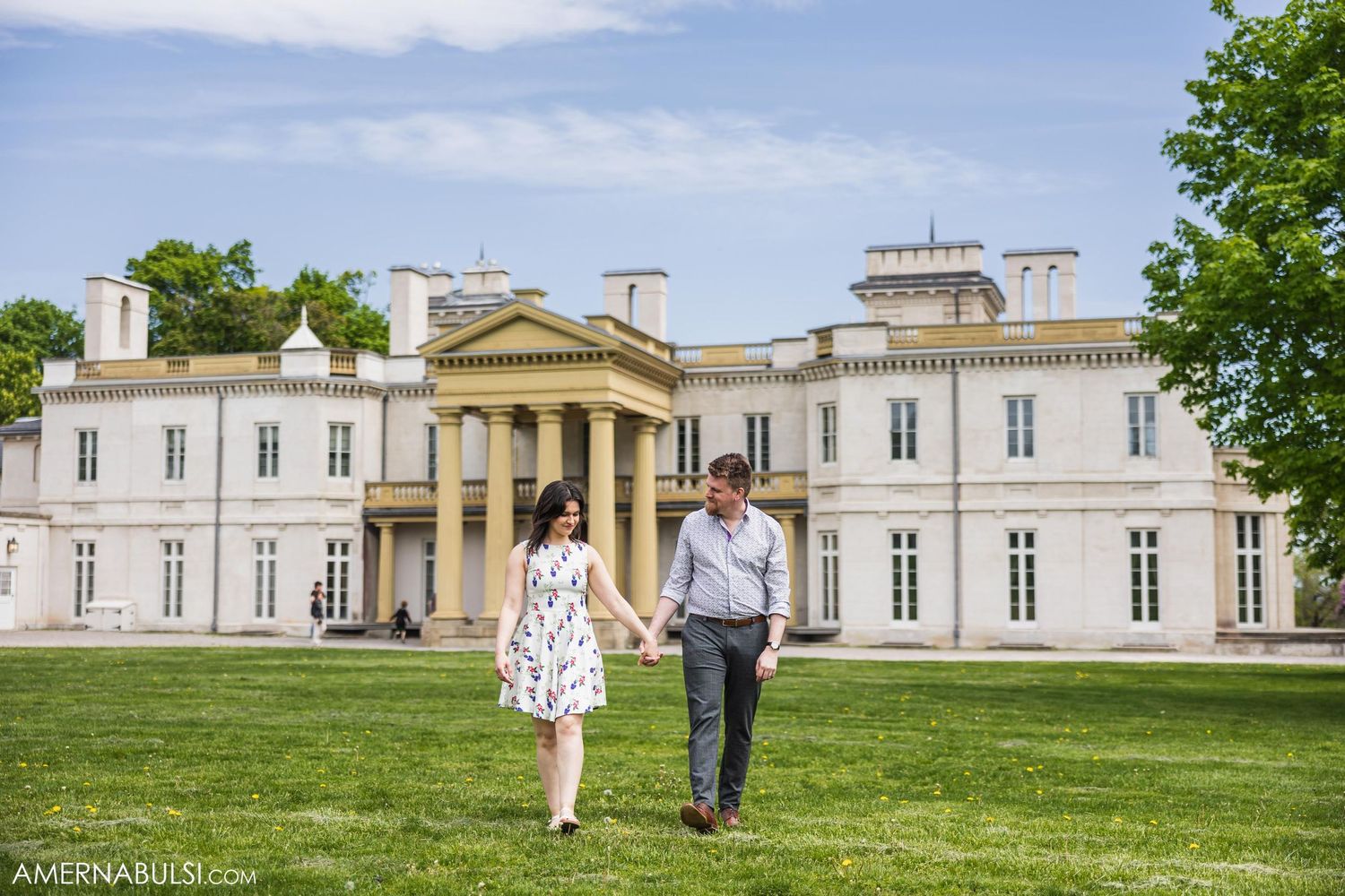 Couple walking hand in hand in front of a grand white mansion with neoclassical architecture.