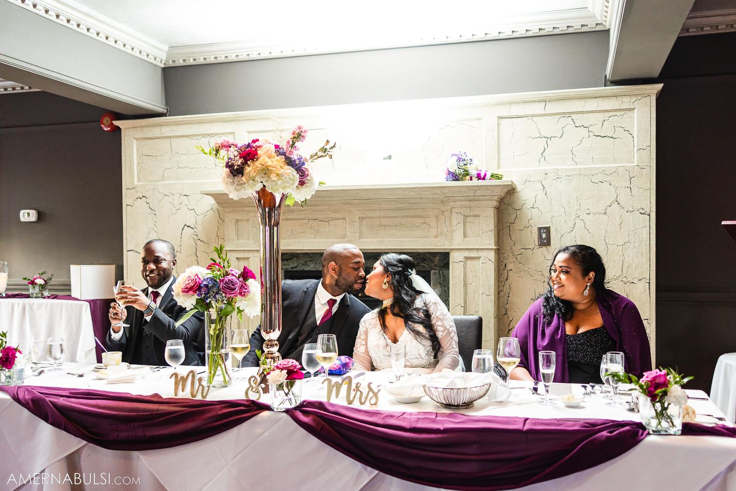 Wedding reception table decorated with purple accents and tall floral centerpieces.