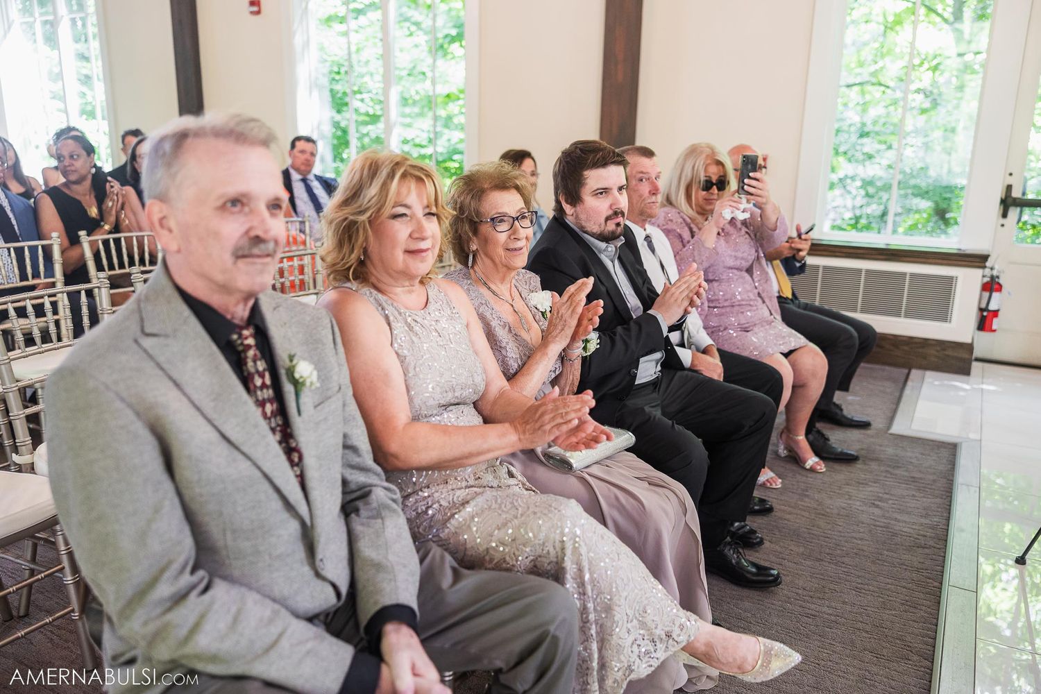 Wedding guests in formal attire seated in rows of chiavari chairs during ceremony.