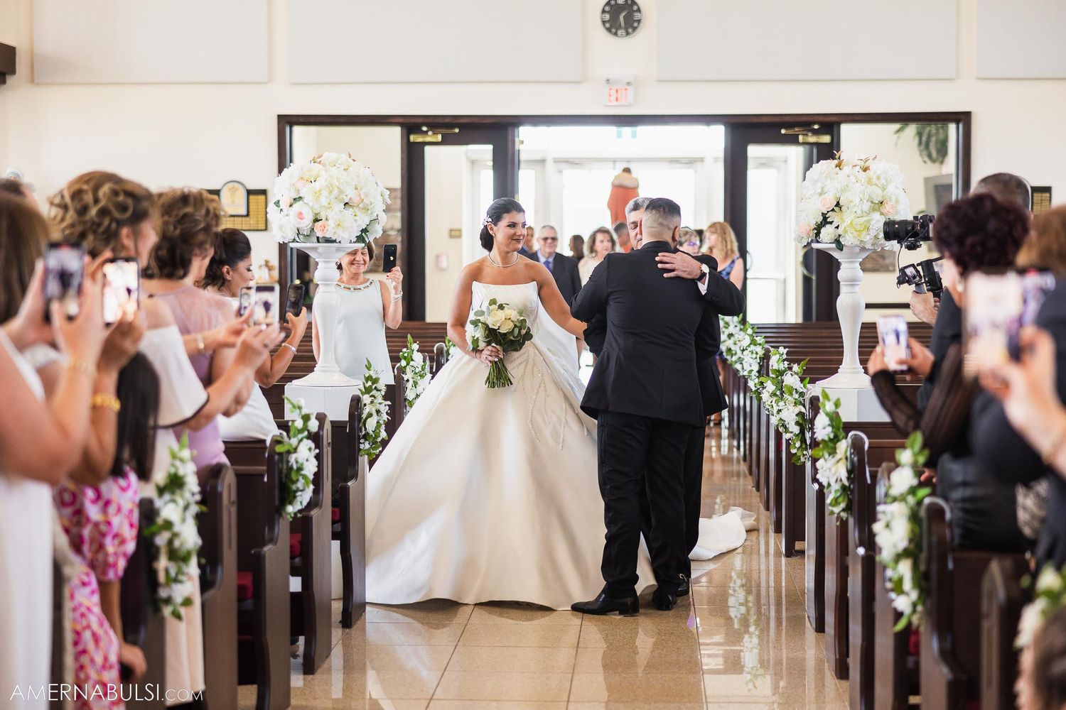 Guests line the church aisle taking photos during the wedding ceremony processional.