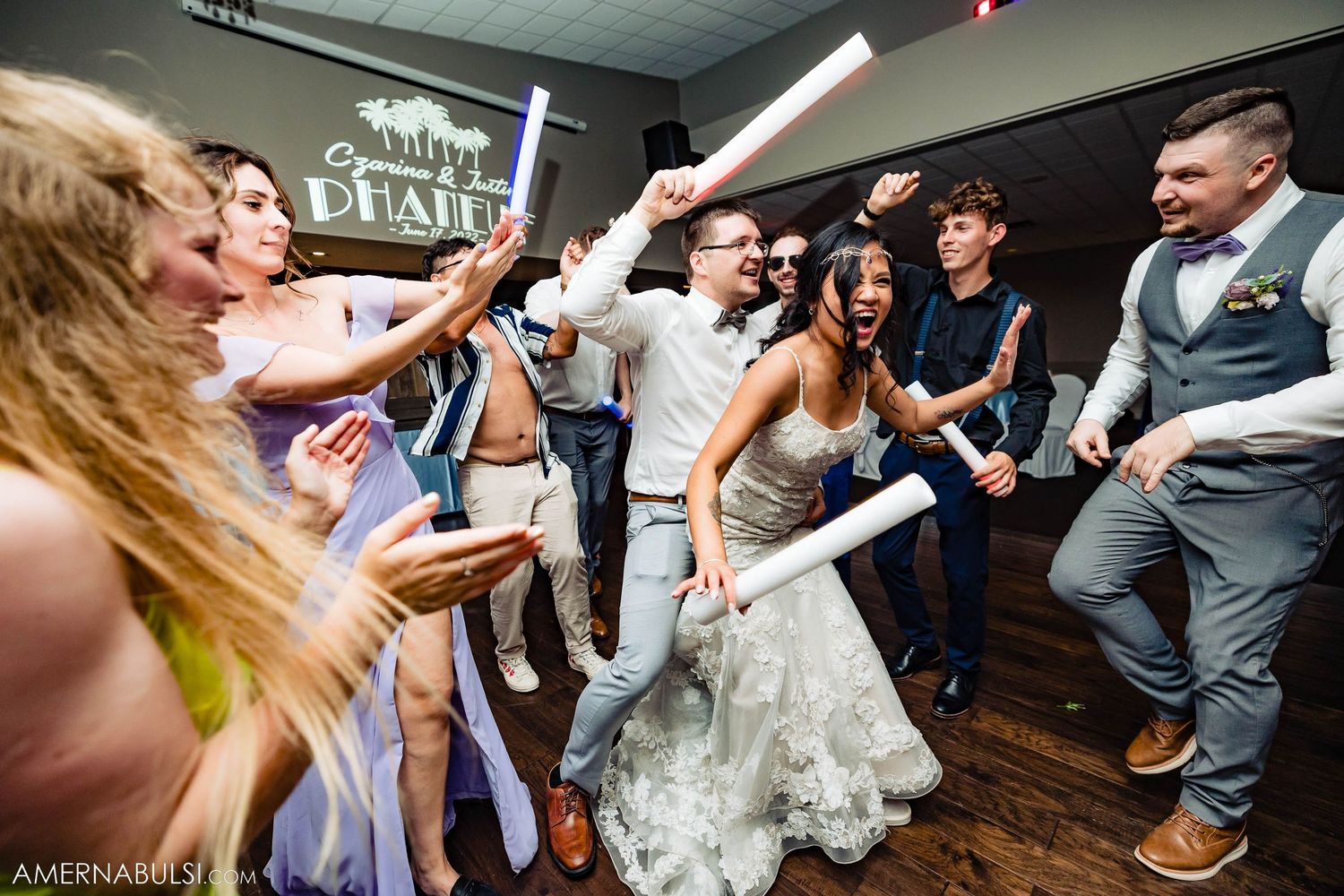 Celebration on dance floor with wedding guests and attendees cheering with arms raised.