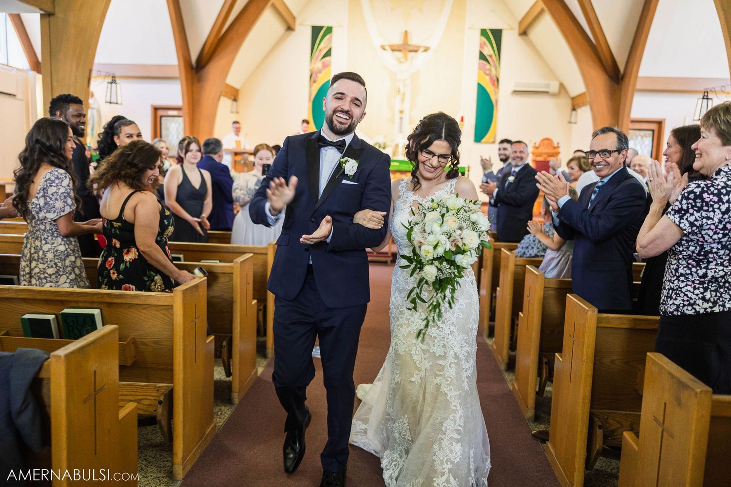 Joyful couple walks down church aisle after wedding ceremony while guests clap and celebrate.